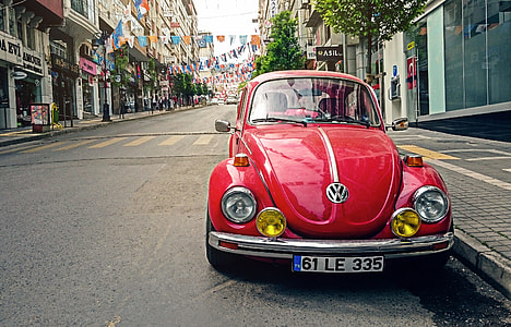 red Volkswagen Beetle car park beside concrete buildings