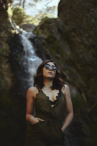 woman wearing black sunglasses, black scooped neck dress near in waterfalls during day time