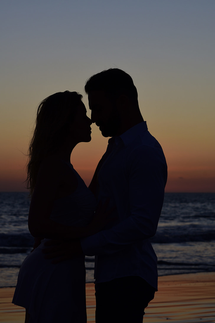 silhouette of man and woman standing side by side near beach during dusk