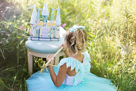 white and blue castle toy and girl wearing blue and white sleeveless tutu dress at daytime
