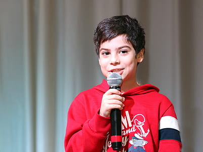 boy wears red hoodie and holds talking white holding black microphone