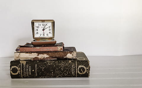 brown analog clock with books