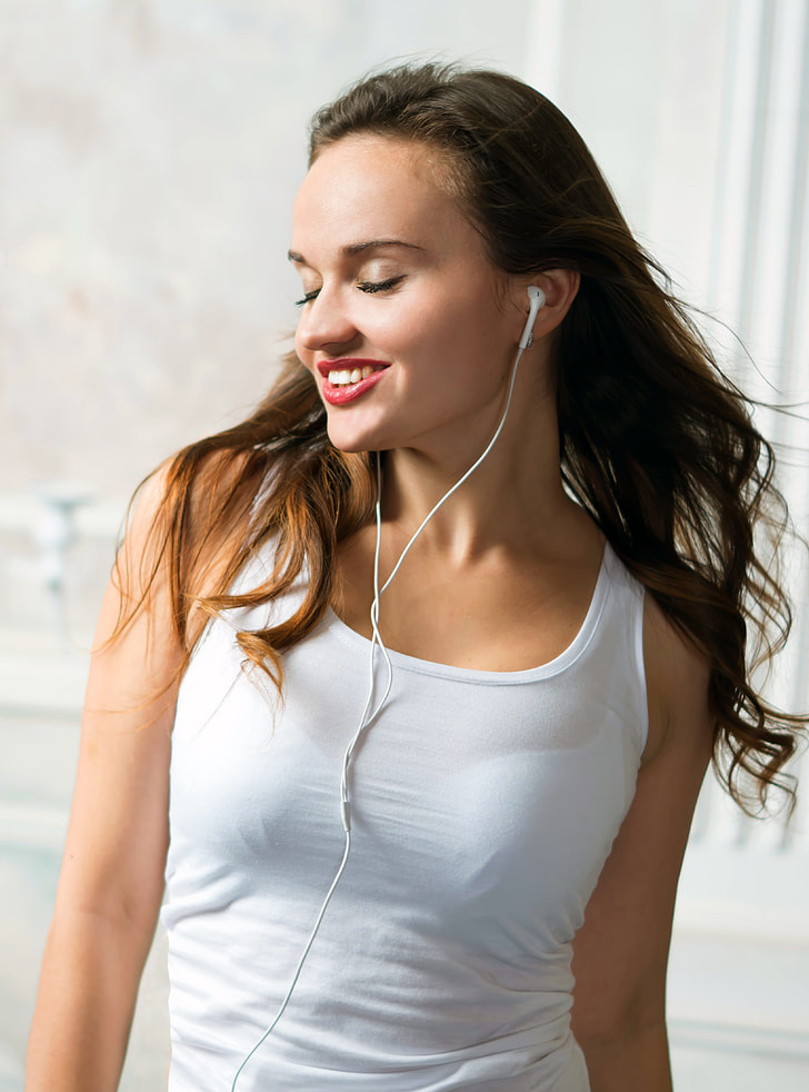 woman wearing white tank top and white earphones standing inside well lighted room
