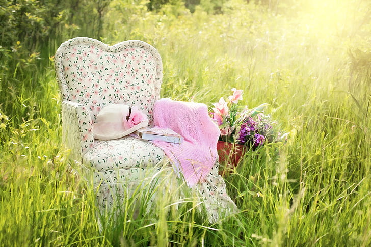 white, green, and pink floral fabric sofa chair with pink textile and hat on grass
