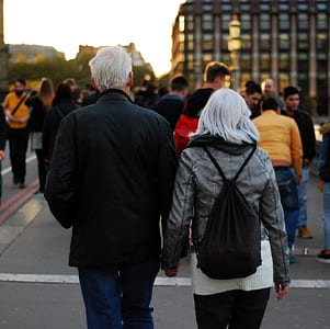 Man in Black Jacket Beside Woman in Grey Leather Jacket Holding Hands at Dusk in Busy Street