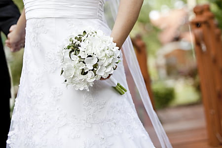 person wearing white dress while holding white petaled flower bouquet