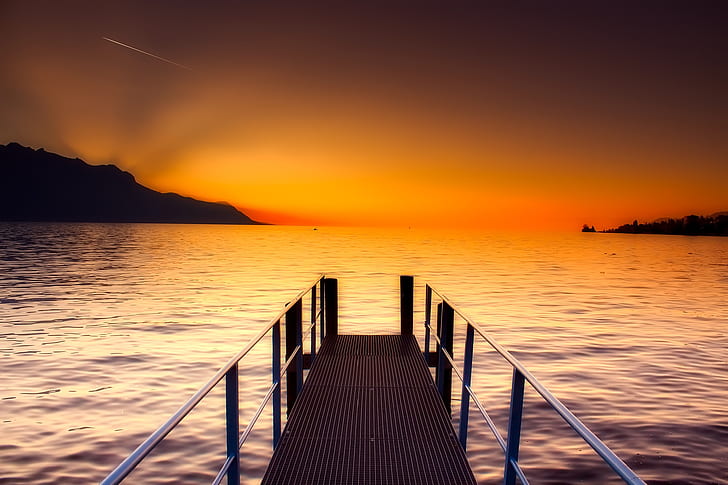 wooden dock on body of water with silhouette of mountains at distance