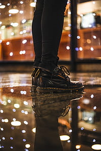 Photo of Person Wearing Black Fitted Jeans and Black Dr.martens Boots Standing on Black Floor Tiles