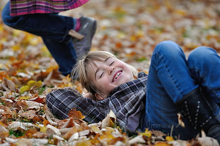 girl in black and brown plaid shirt with blue jeans lay on dried leaves