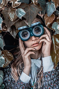 close-up photography of woman in long-sleeved top wearing goggles surrounded of leaves