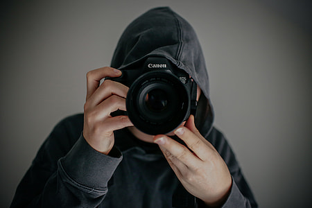 person wearing gray hoodie holding Canon DSLR camera