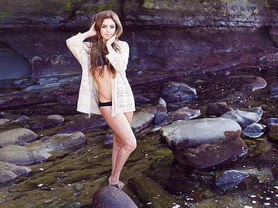 woman wearing bikini top and panties with cover up standing on body of water near rocks