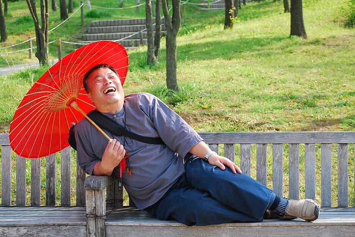 man laughing while sitting on bench holding oil paper umbrella