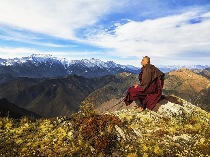 man sitting on stone near mountain range