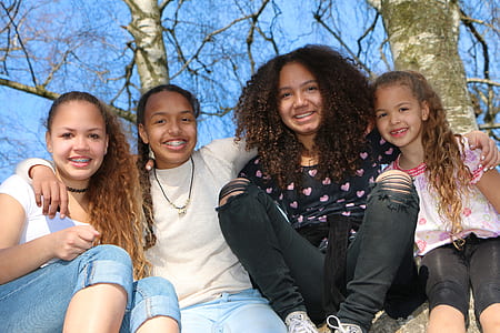 four girl sits on rock behind bare tree at daytime