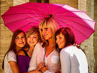four women wearing clothes standing under pink umbrella