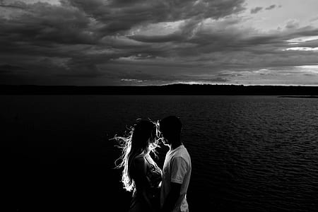 grayscale photo of man and woman kissing beside the body of water