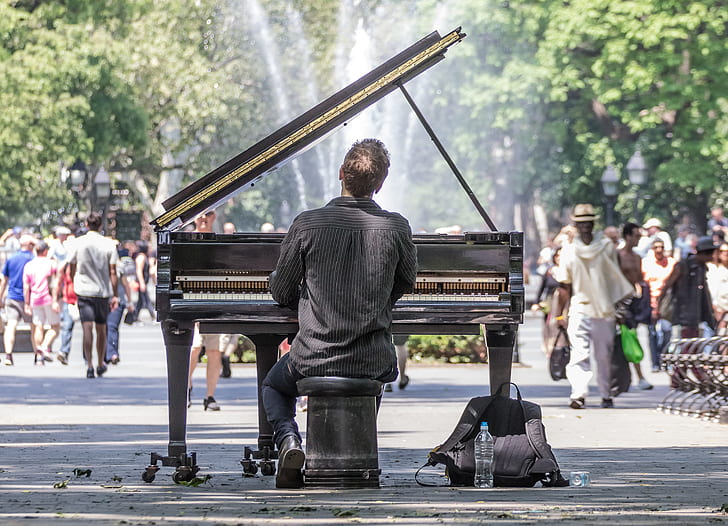 back view of man playing grand piano in front of people
