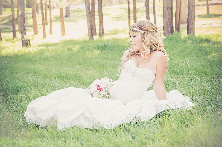 woman wearing white sweetheart neckline wedding dress sitting on green grass during daytime