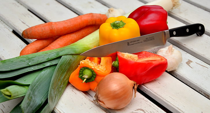 red and yellow bell peppers carrots and onion with black handle kitchen knife
