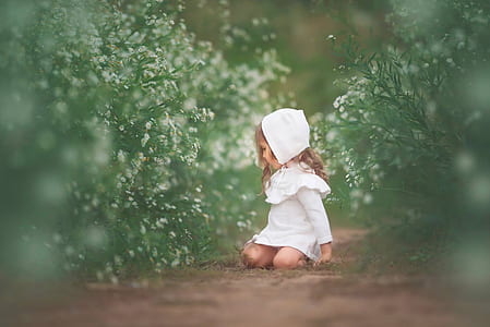selective focus photography of girl wearing white dress lying between green leaf plants at daytime