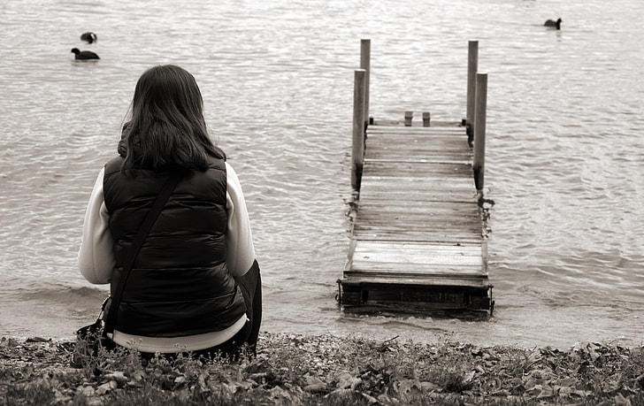 person sitting near body of water and bridge