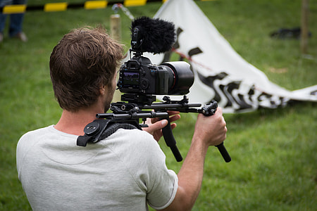 man in white shirt recording video using black DSLR camera during daytime