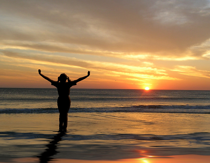 silhouette photo of a woman spreading her hands near seashore during golden hour