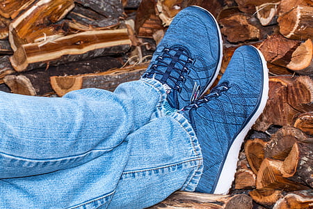 person in blue low-top sneakers leaning on fire woods