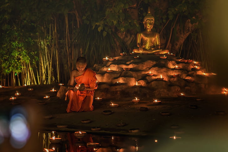 man wearing monk suit behind Gautama statue during nighttime