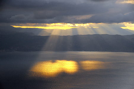 sun rays on body of water during dark clouds