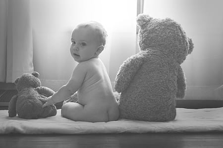 grayscale photo of naked baby sitting next to two teddy bears