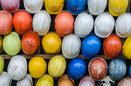assorted color of hardhats piled on brown wooden rack