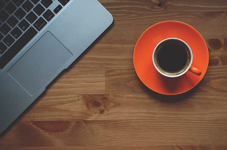 cup of coffee beside gray laptop on brown wooden desk