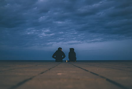 silhouette of two person sitting on ground under gloomy skies