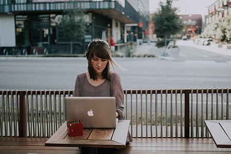 woman in grey 3/4 sleeve top facing MacBook on brown table