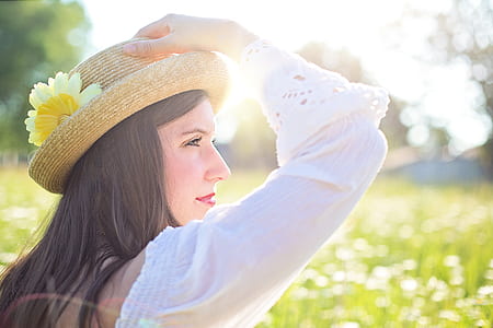 woman wearing white long-sleeved blouse holding her brown hat with yellow flower