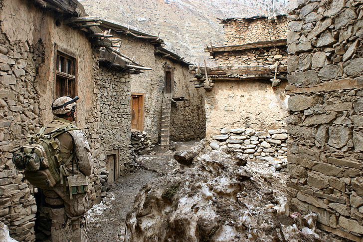 male soldier in gear set standing in front of rocky buildings
