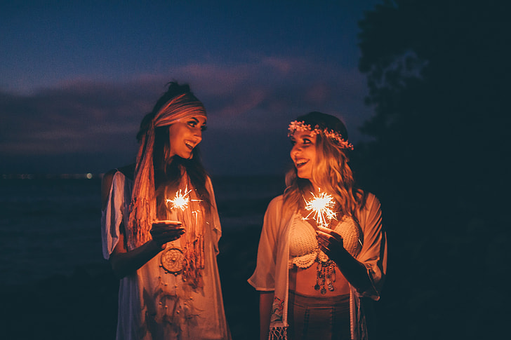 Two women smile at sunset holding sparklers