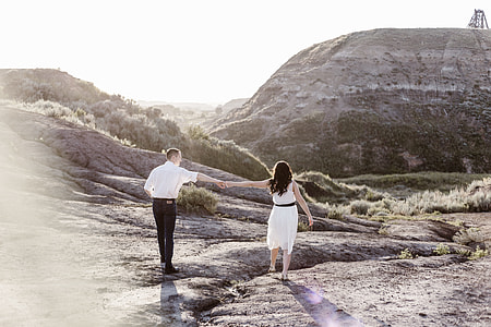 man and woman holding hands while walking on gray mountain during daytime