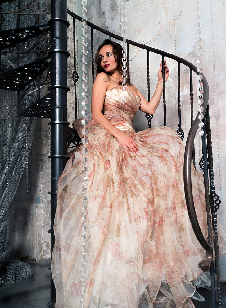 woman in white, red, and brown strapless dress sitting on black metal spiral stairs