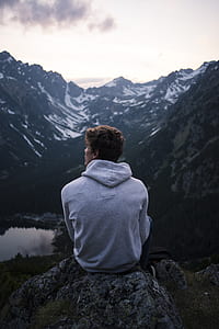 photo of man sitting on rock facing mountain