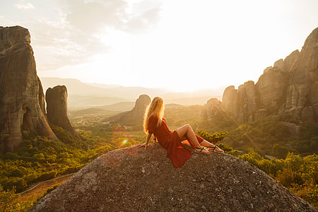 woman wearing red dress sitting on rock formation at daytime