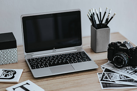 Black-and-white photos with a silver laptop, a smartphone, car keys, pencils and a camera