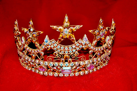 gold-colored crown with assorted-color gemstones on red textile