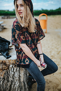 Beautiful blonde woman relaxing with a can of coke on a tree stump by the beach