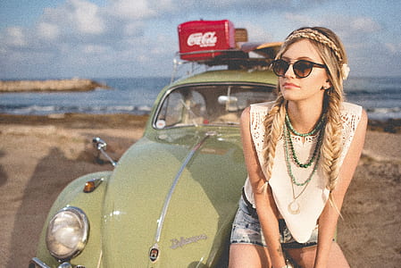 woman sitting in front of green Volkswagen Beetle on beach sand during daytime