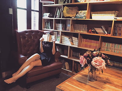 woman wearing black mini dress reading a book at the library