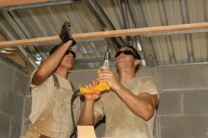 man wearing gray crew-neck t-shirt using yellow corded hand drill