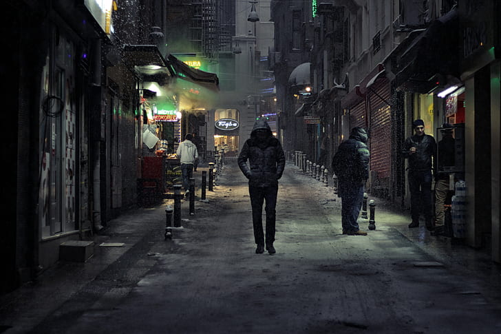 man in black hoodie walking beside concrete building at nighttime